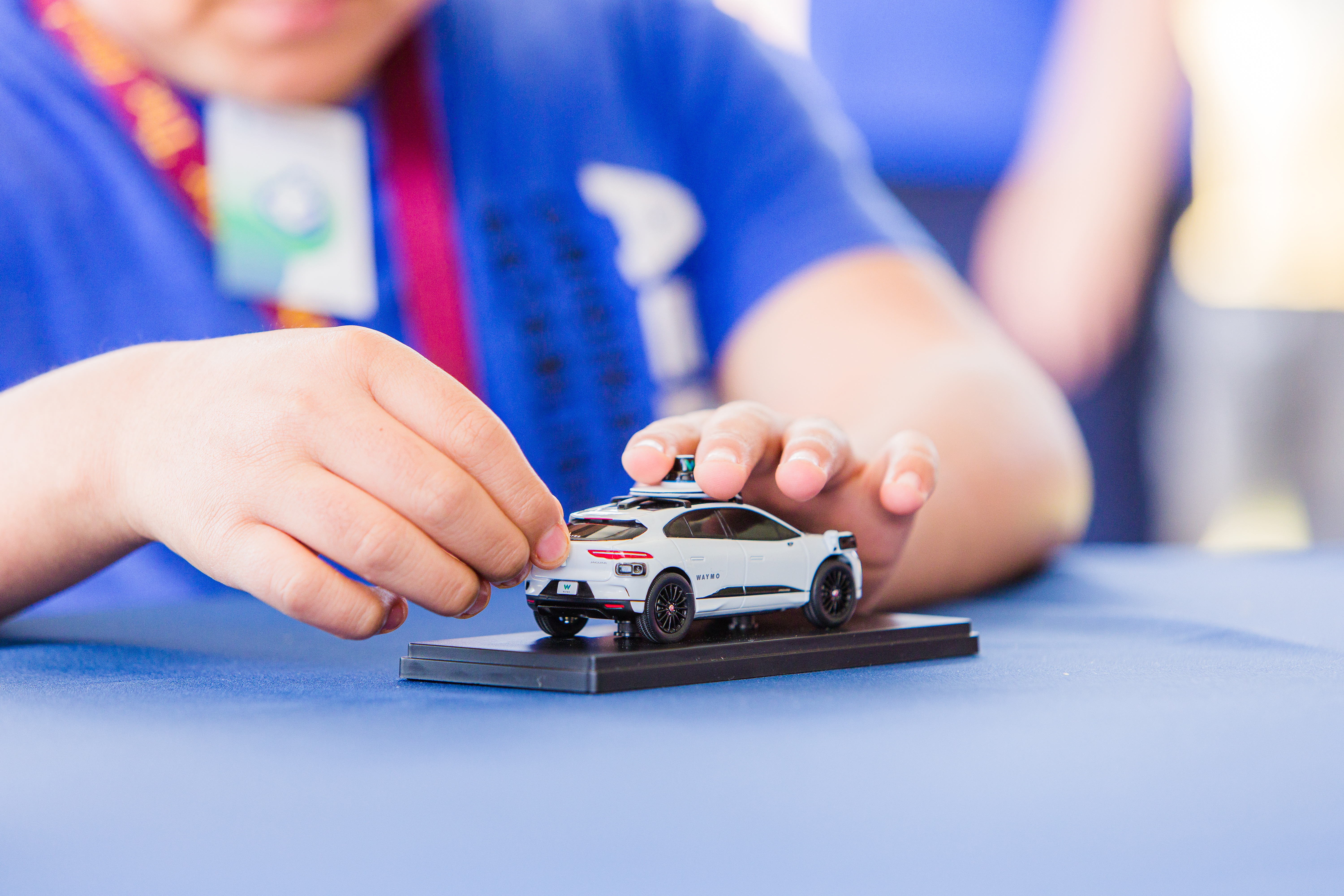 A student feels the outline of a small Waymo vehicle model on a table
