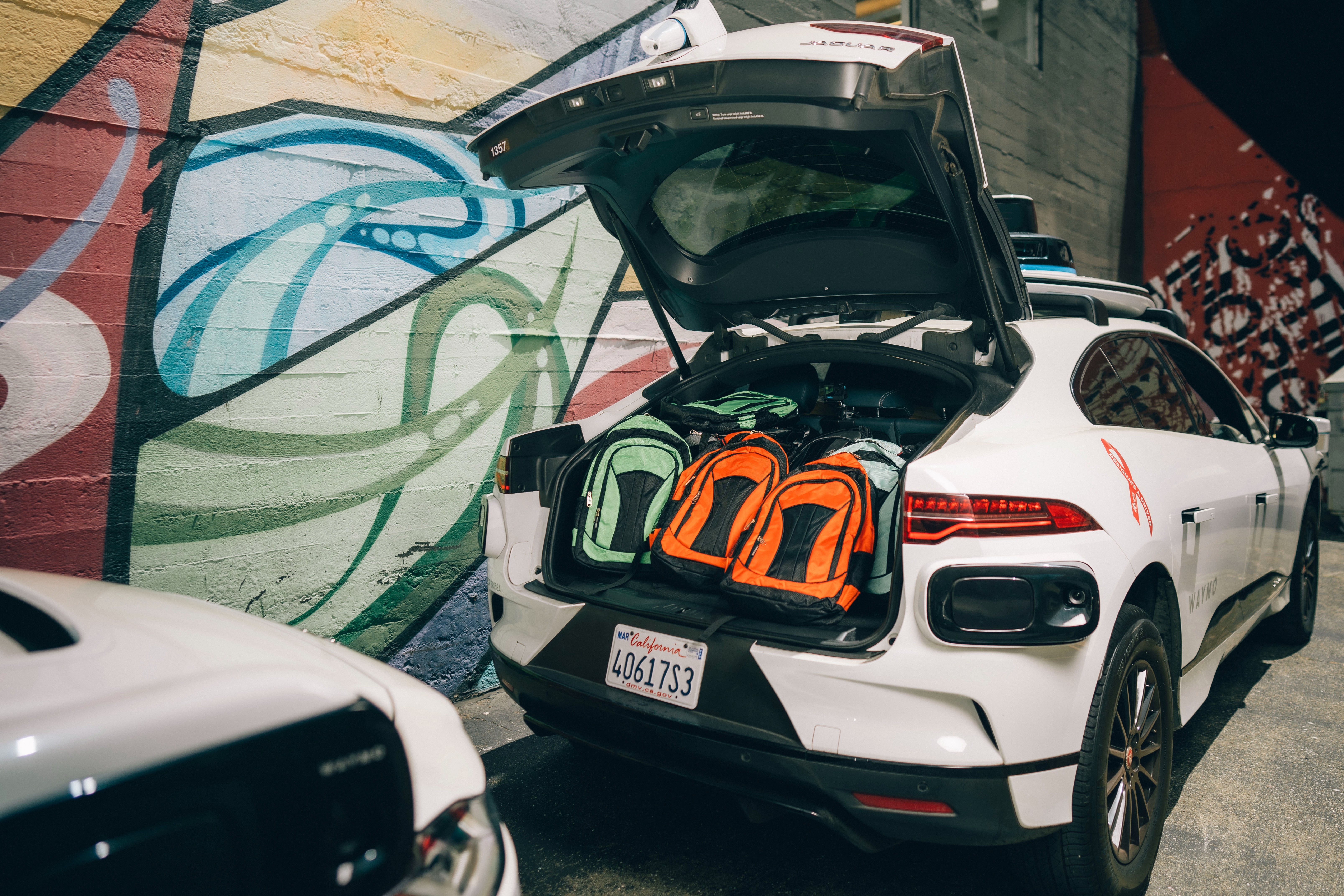 Waymo Vehicle parked in front of a mural with a trunk full of brightly colored backpacks
