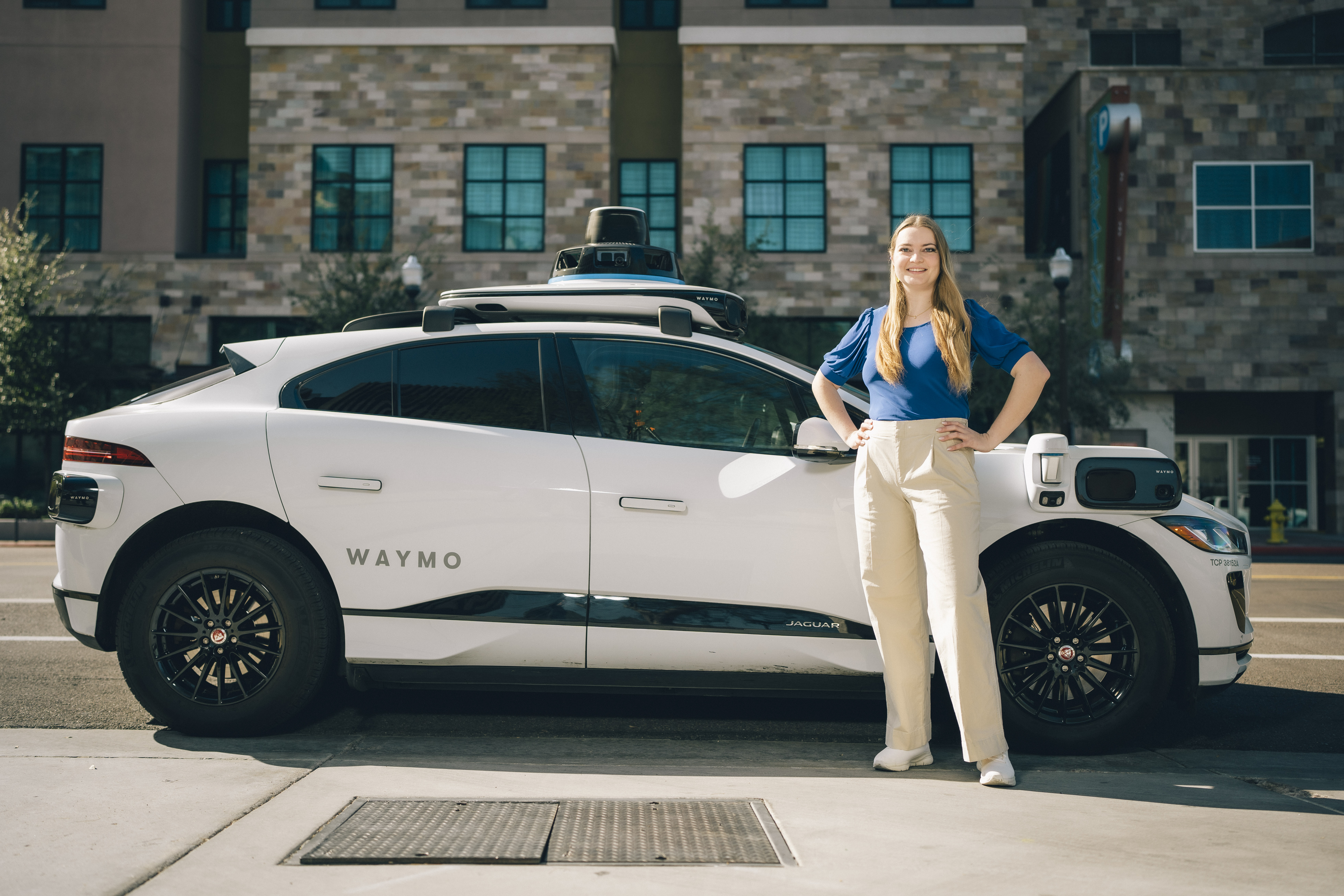 Anne Dorsey standing on the sidewalk, posing in front of a Waymo vehicle