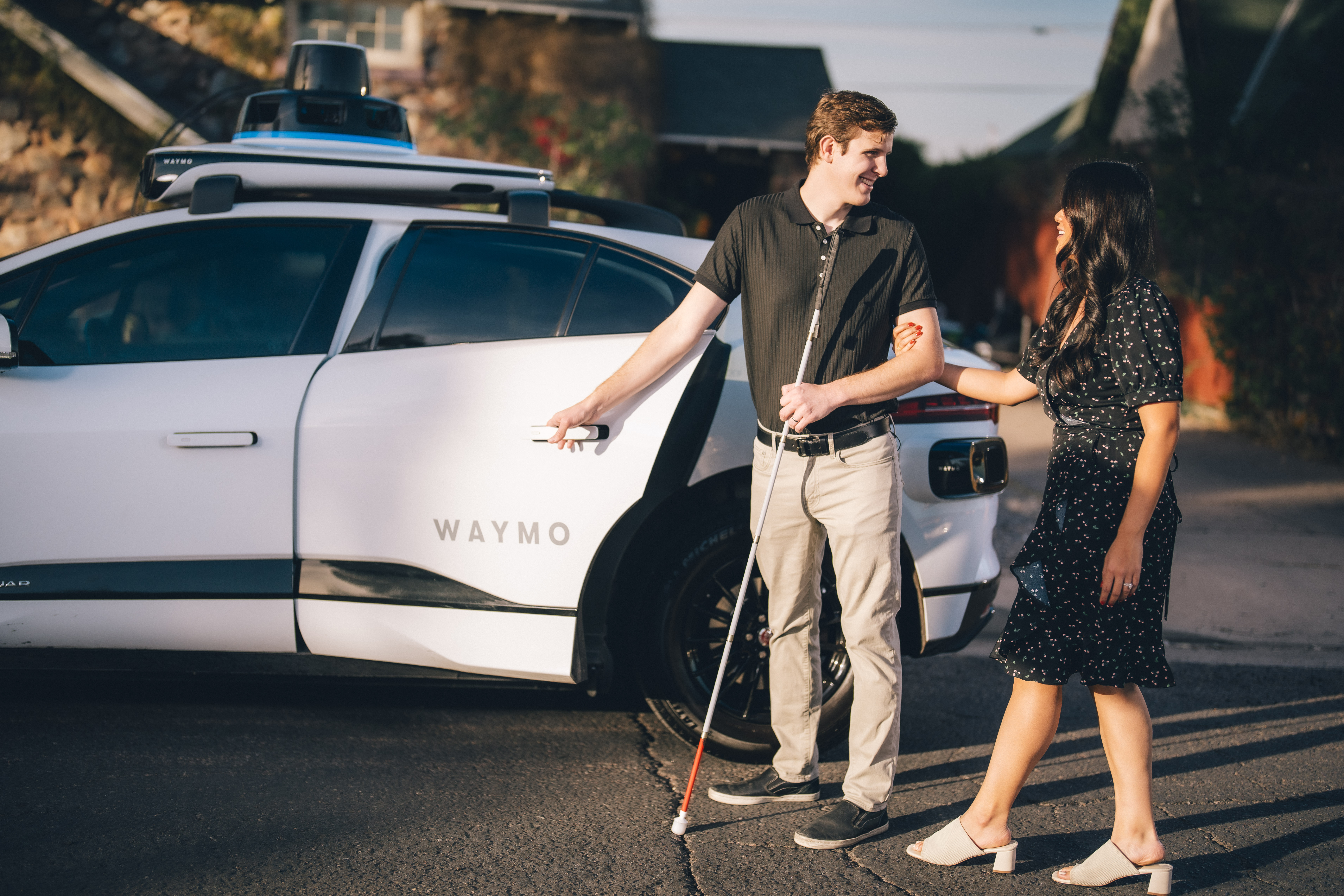 Lilian holding onto Max's arm as he opens the door to a Waymo One autonomous vehicle