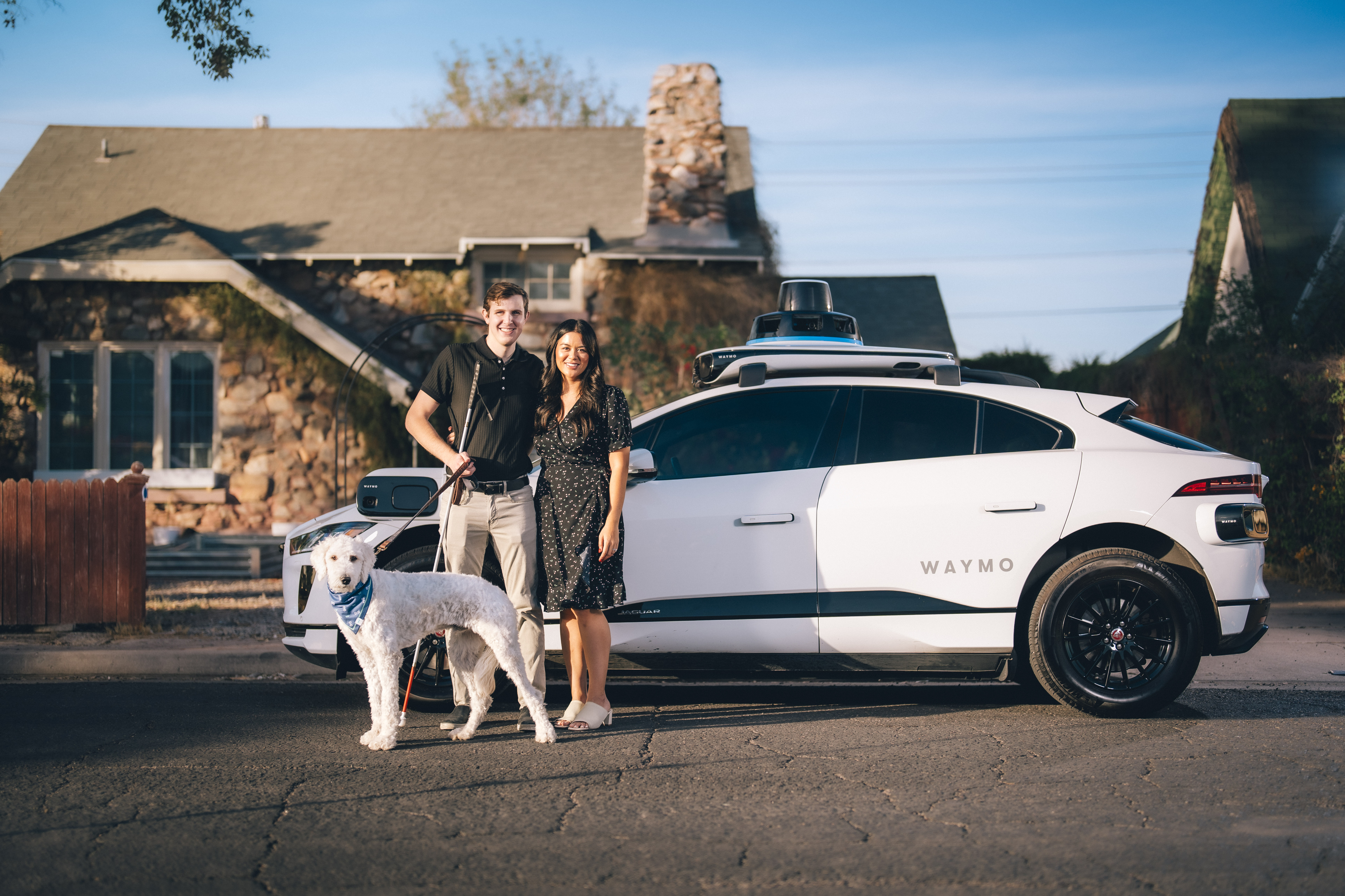 Max and Lilian posing with their dog in front of a Waymo One autonomous ride-hailing vehicle