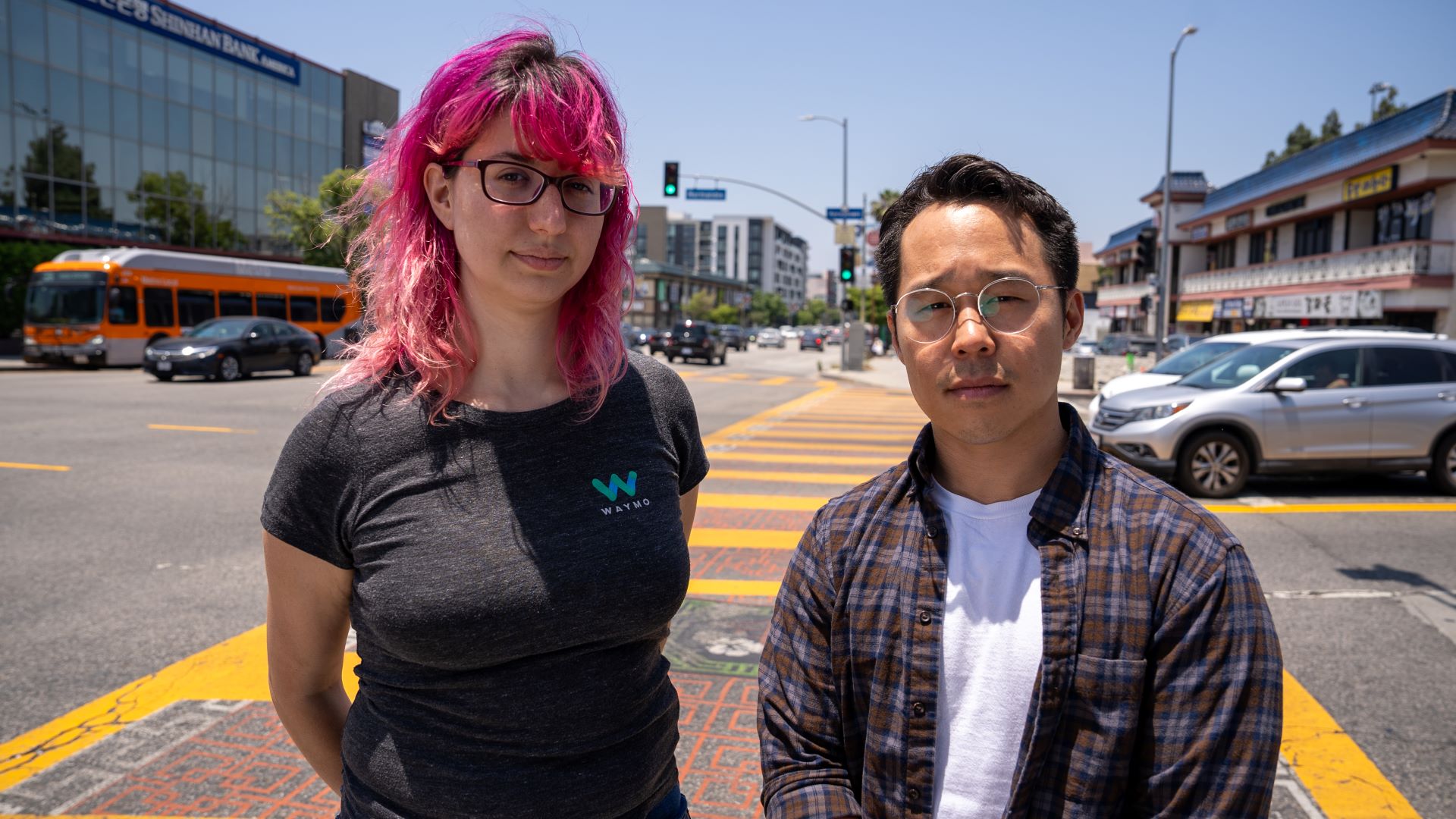 Waymo engineer and LA Walks executive director stand side-by-side on the corner of a busy intersection of Koreatown, Los Angeles