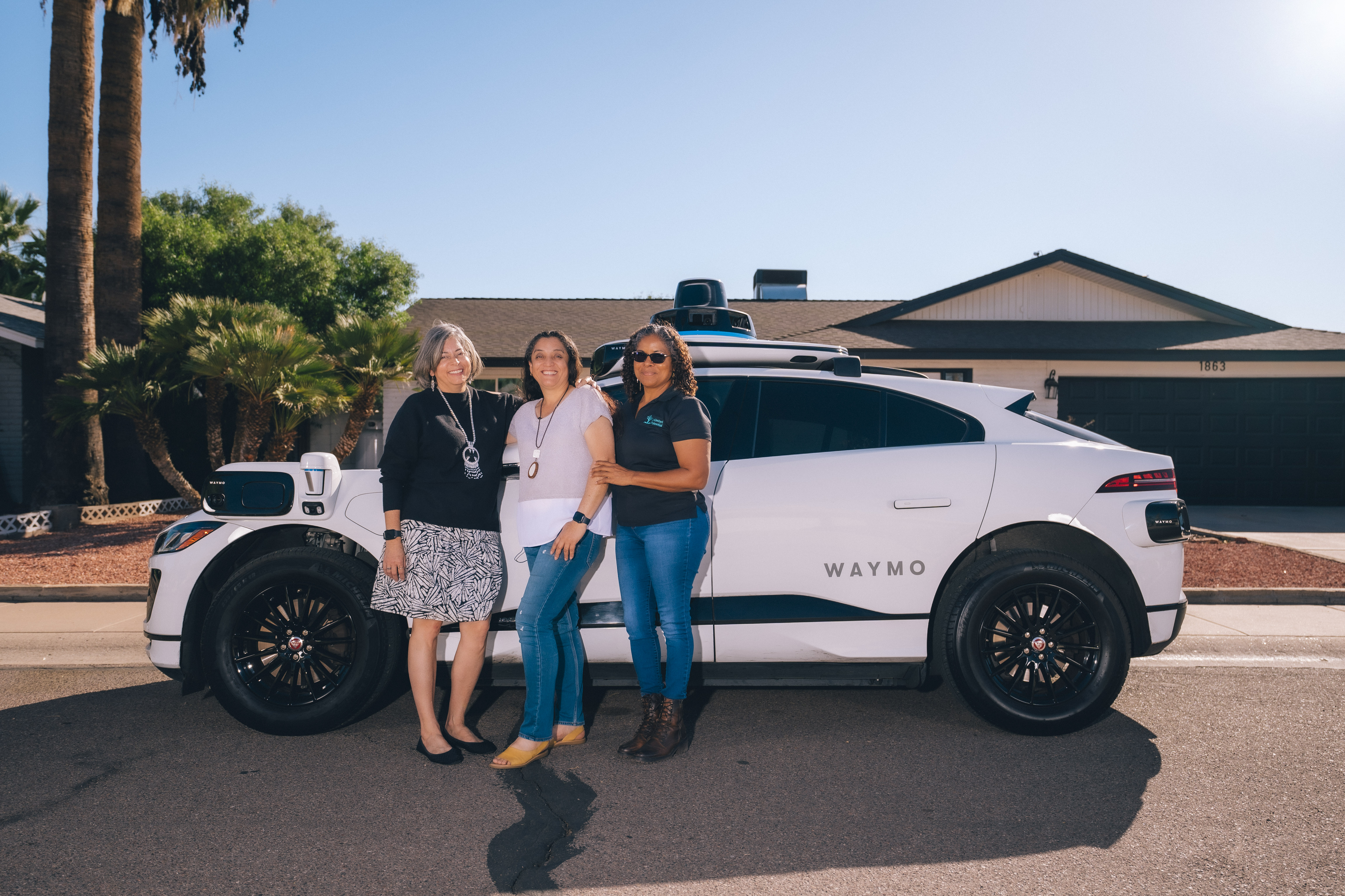 Emma, Juana, and Minerva from Unlimited Potential stand alongside a Waymo One ride-hailing vehicle