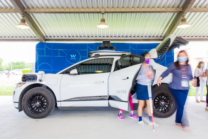 Three women, one with a cane, getting out of a parked Waymo vehicle