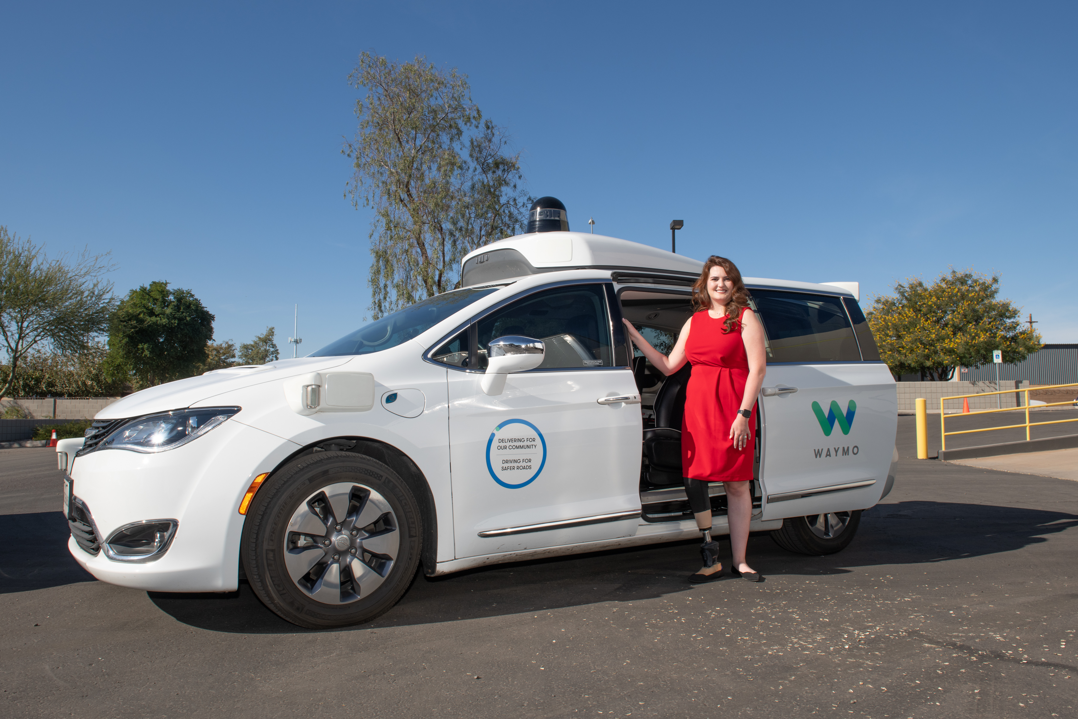 Woman in red dress standing in front of a Waymo autonomous vehicle