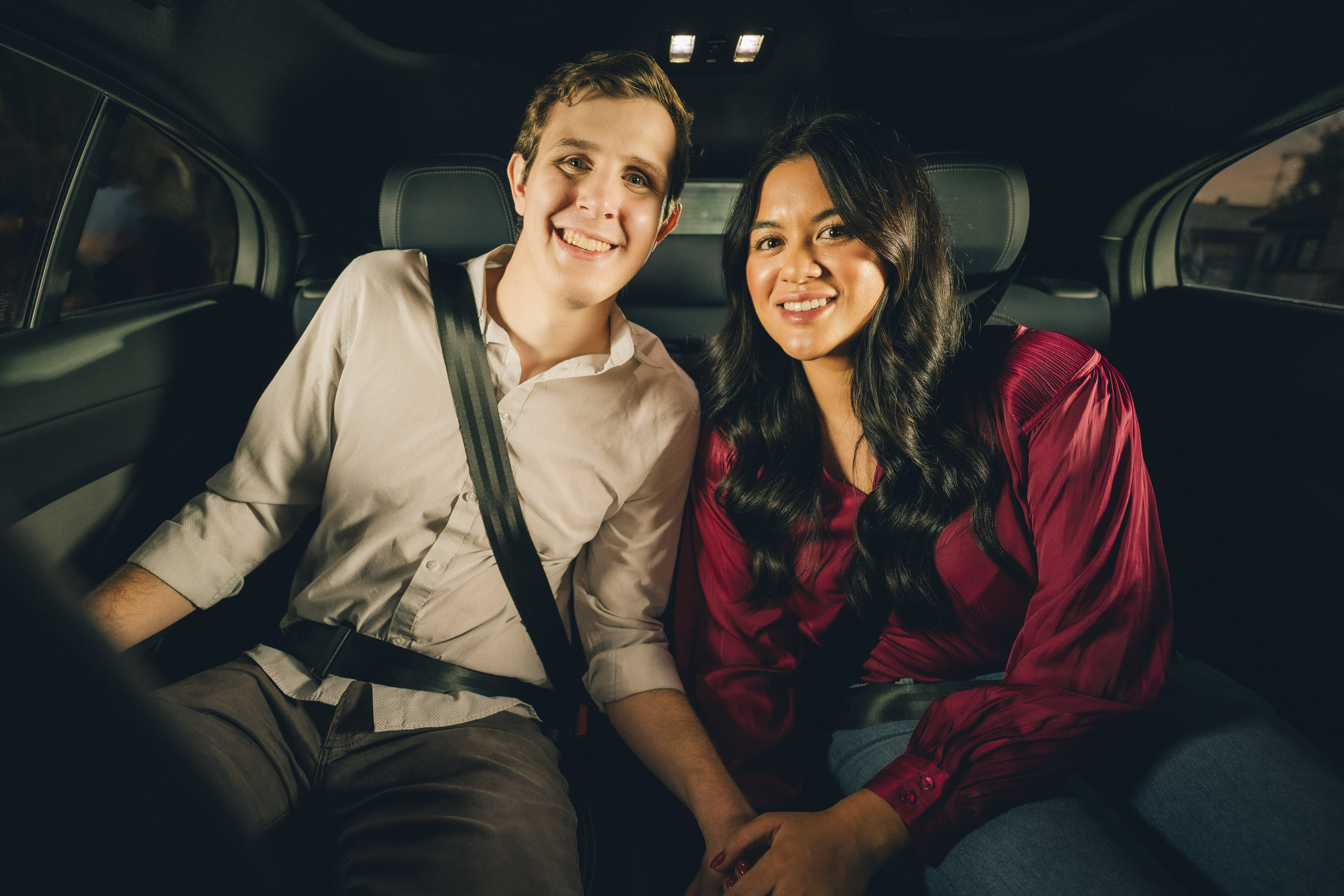 Max and Lilian holding hands and smiling in the backseat of a Waymo One autonomous ride-hailing vehicle
