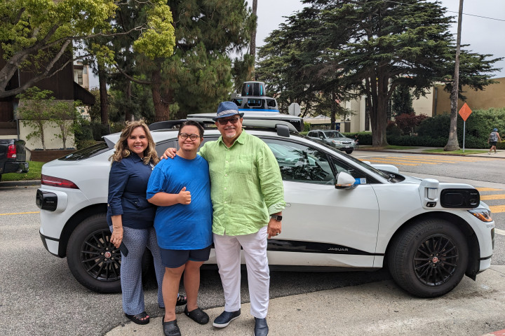 Fernando Gomez, co-founder of Integrated Community Collaborative, stands with with his wife and son in front of a Waymo One autonomous vehicle