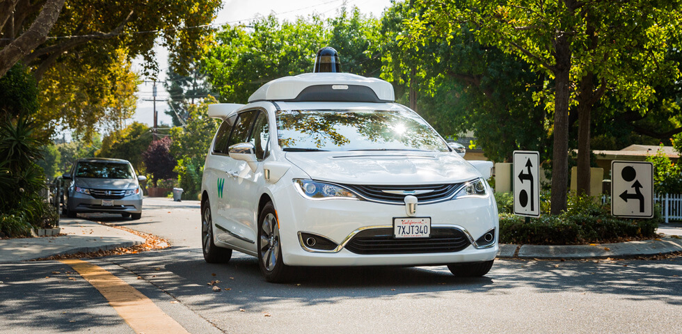 White Waymo vehicle on road lined by trees