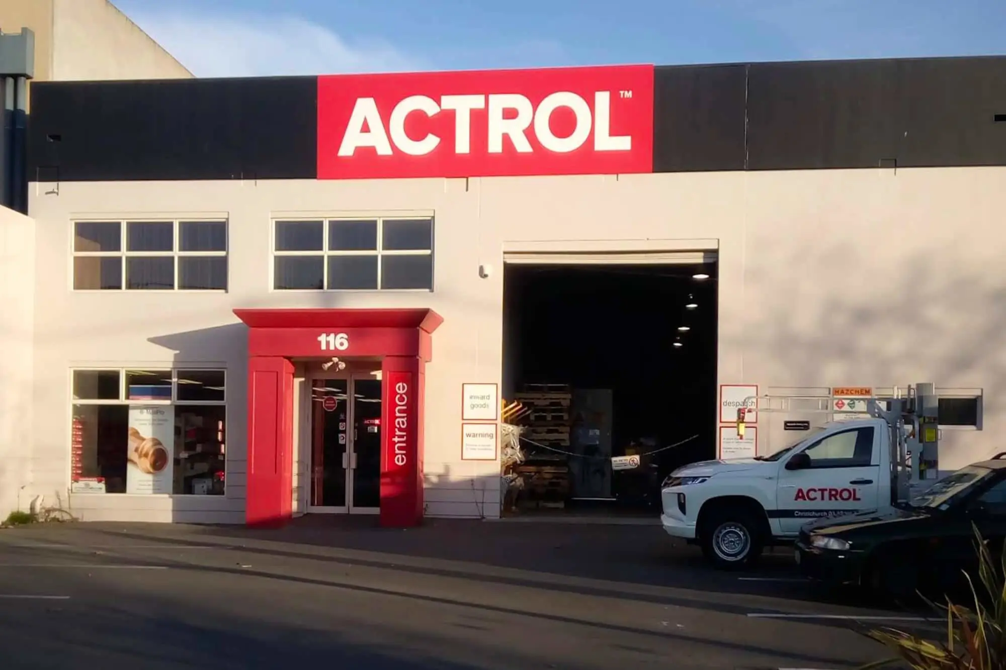 Exterior of an Actrol building with red signage, red entrance marked 116, open garage door, and white truck parked outside.