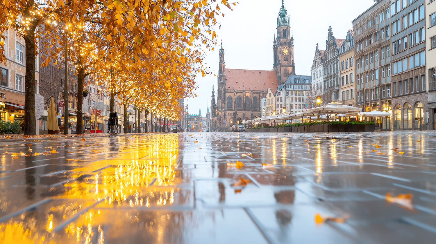 Historischer Stadtplatz mit Herbstbäumen und Spiegelungen auf nassem Pflaster