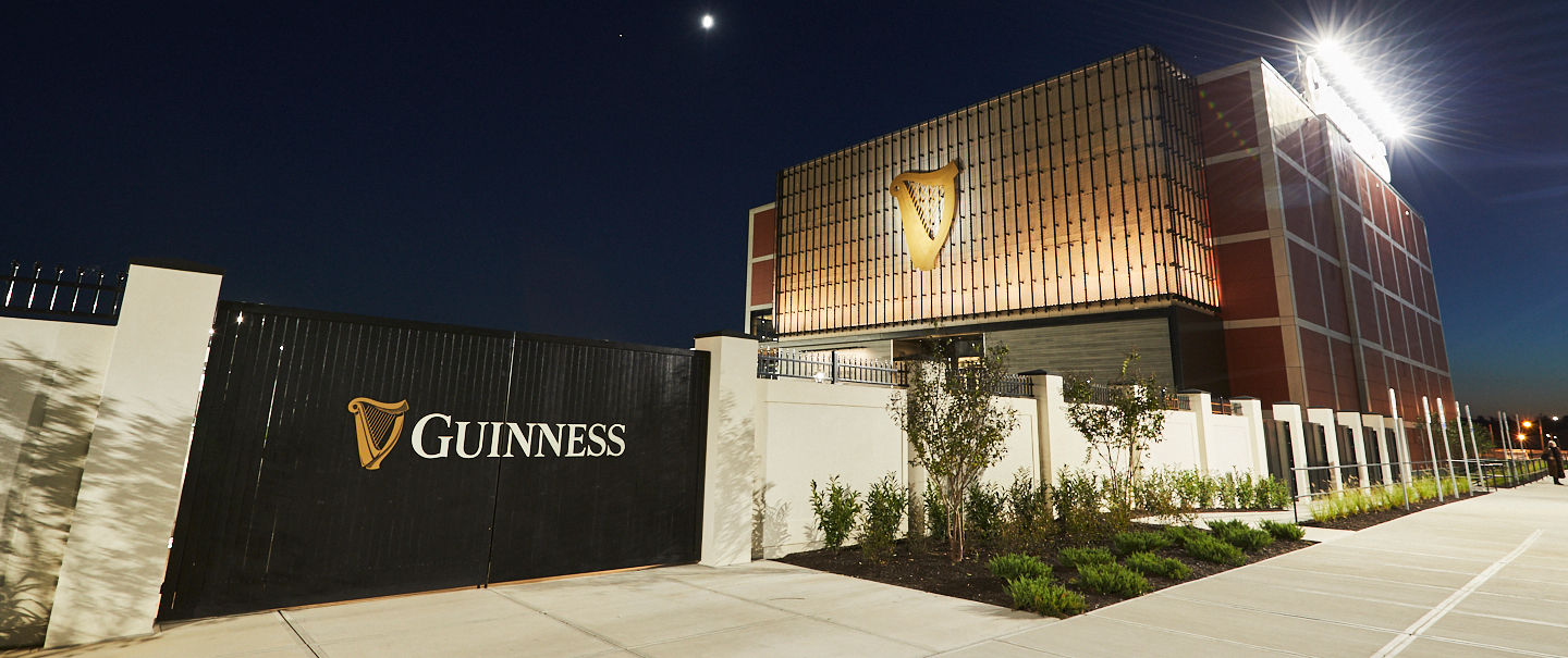 Guinness brewery exterior at night with illuminated harp logo and branded gate