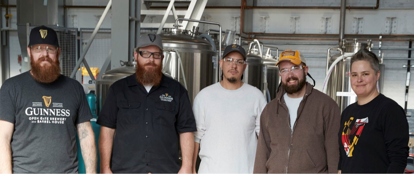 Guinness brewery staff standing in front of stainless steel brewing tanks