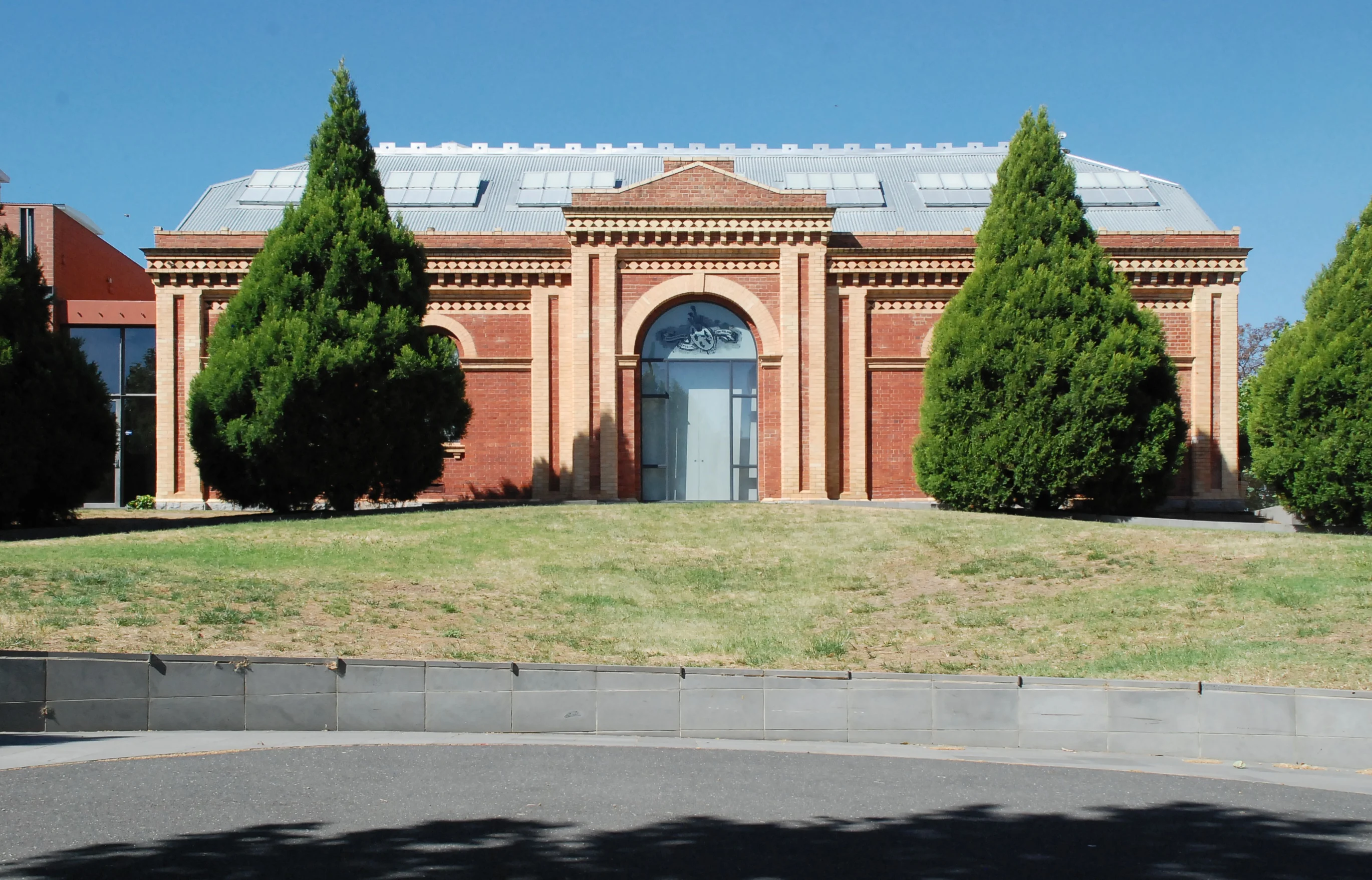 Yellow and bed brick heritage building with trees on either side of the front door