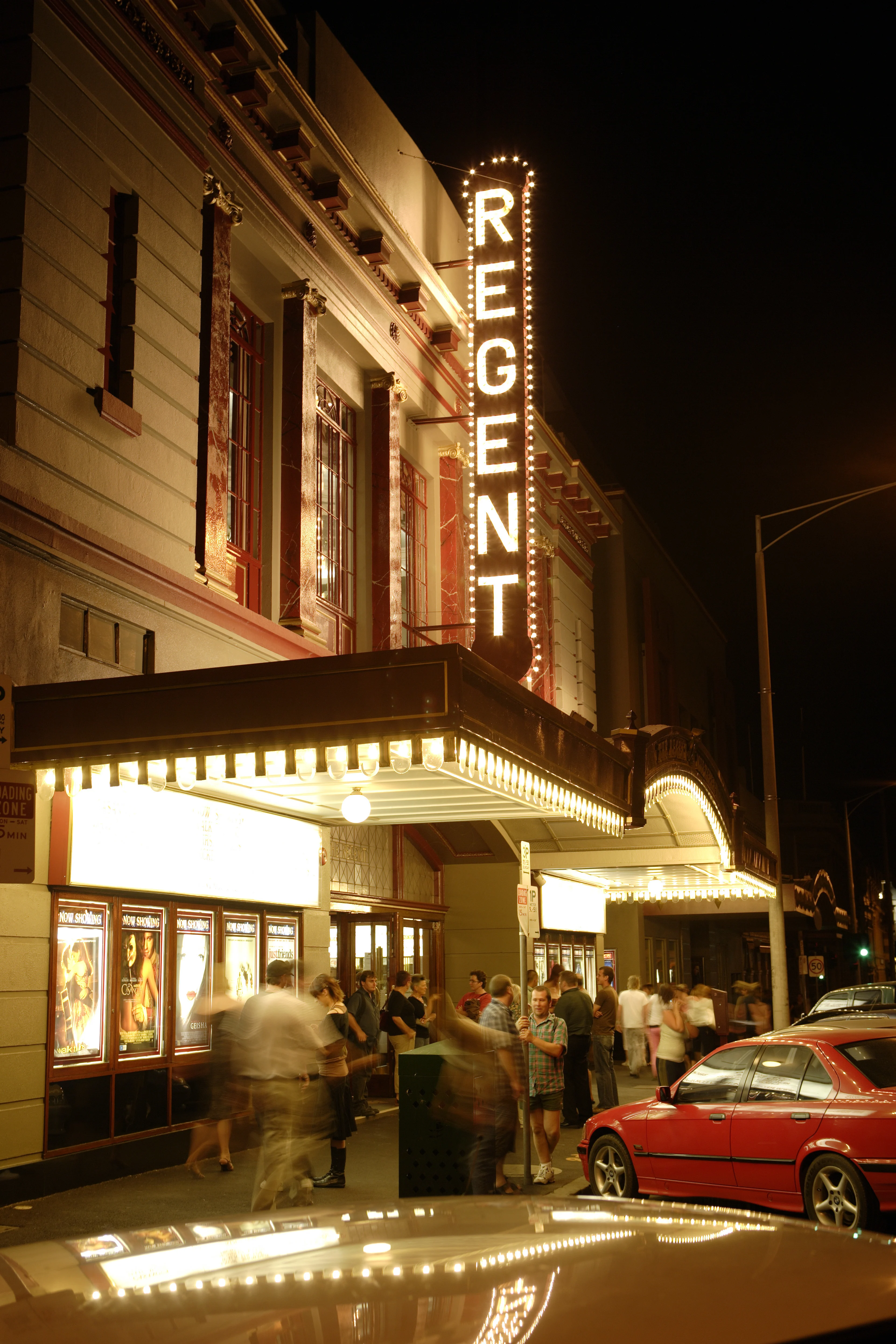 Outside of 1930s style theatre with a glowing vertical sign spelling out "REGENT"