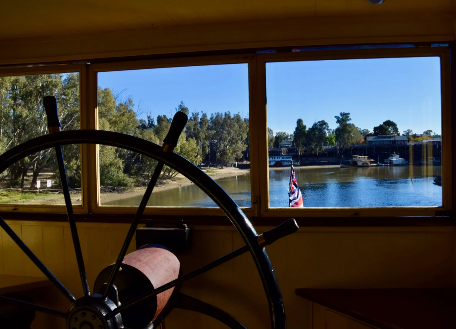 View of the Murray River from window of Paddlesteamer behind steering wheel, Echuca