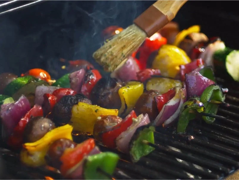 Vegetable skewers on a grill with a basting brush brushing oil