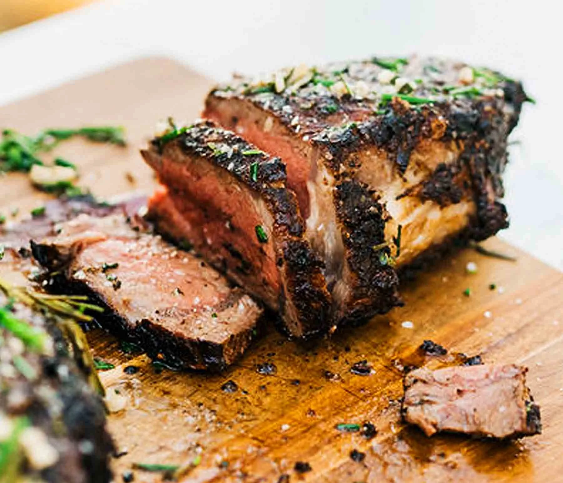 Grilled Ribeye with Shallot Garlic Butter and Basil sliced on a wood cutting board