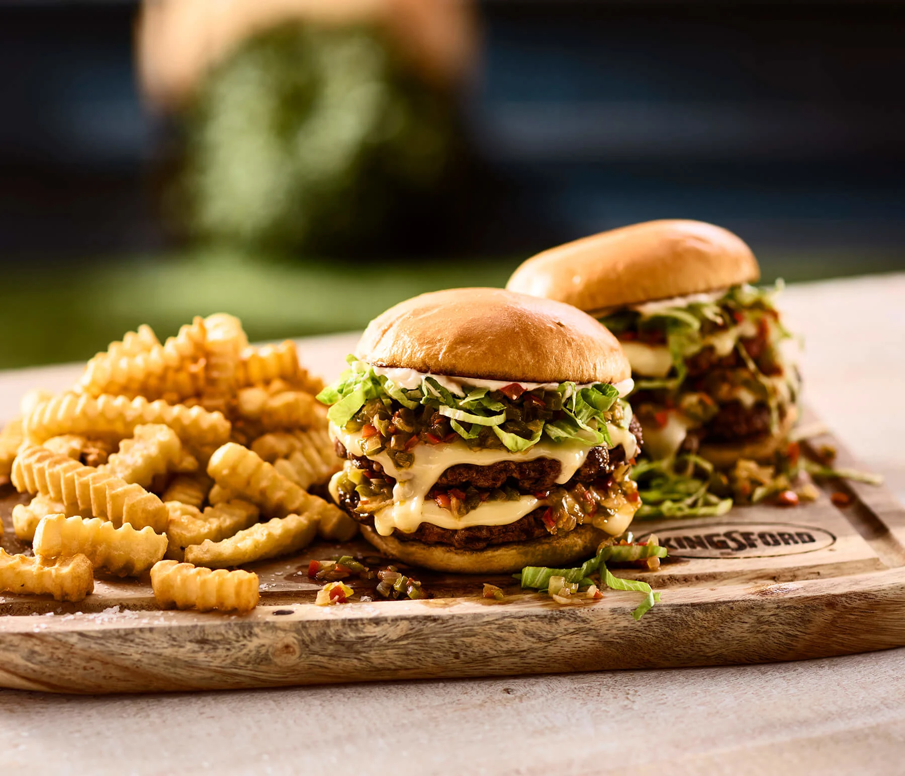 Kingsford™ wooden cutting board with two burgers and crinkle-cut fries.