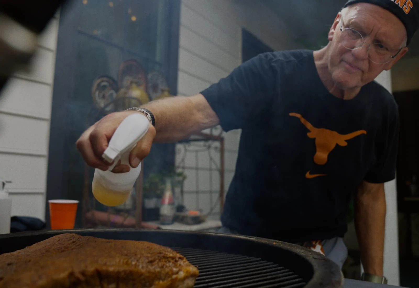 Steven Davis spraying water on a grill with meat cooking on it