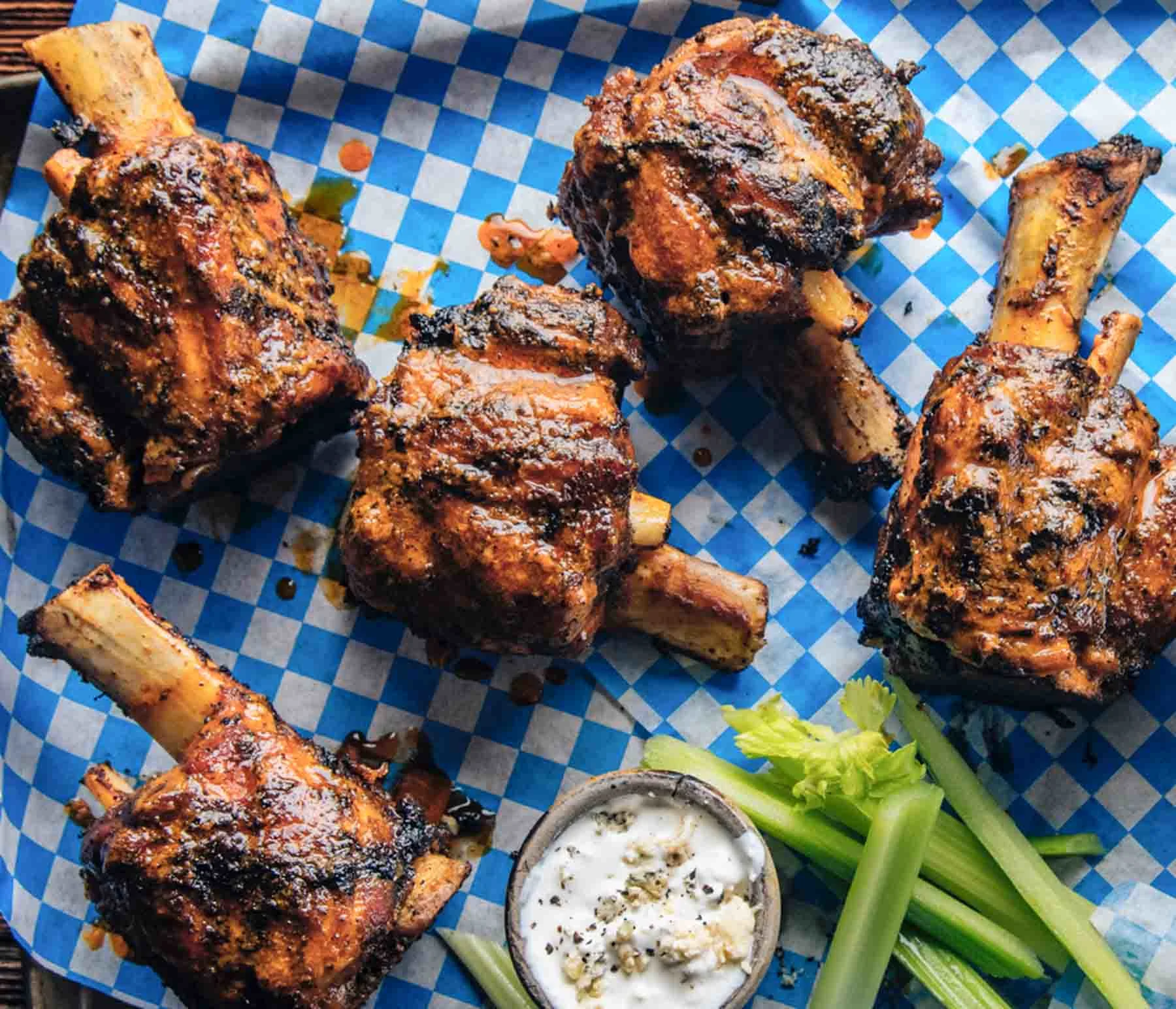 Buffalo wings on checkered blue paper with celery sticks and dipping sauce