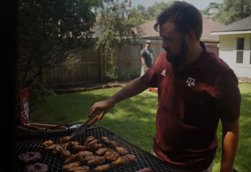 Carter Shelton grilling chicken wings on a grill in a backyard