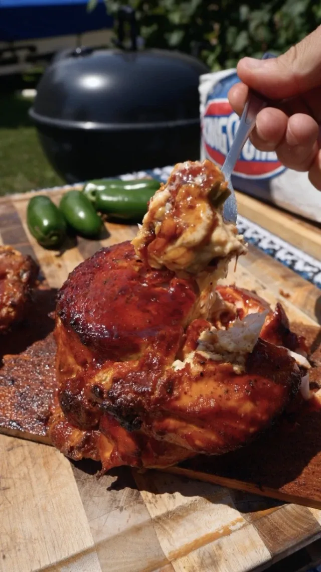 A person taking a large spoonful of food from a grilled salmon, jalapeño peppers and a barbecue in the background