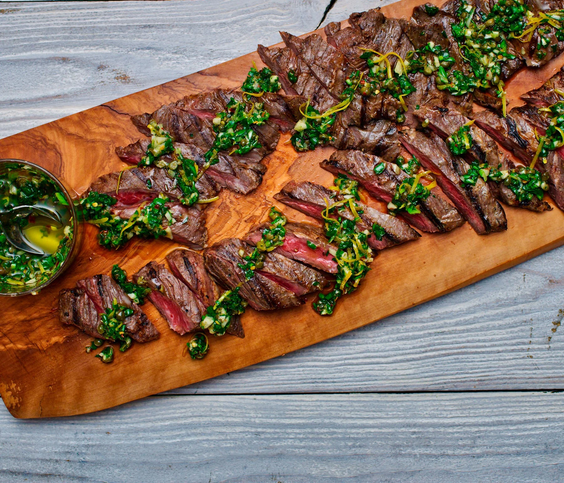 Grilled skirt steak on a wooden board with chimichurri sauce