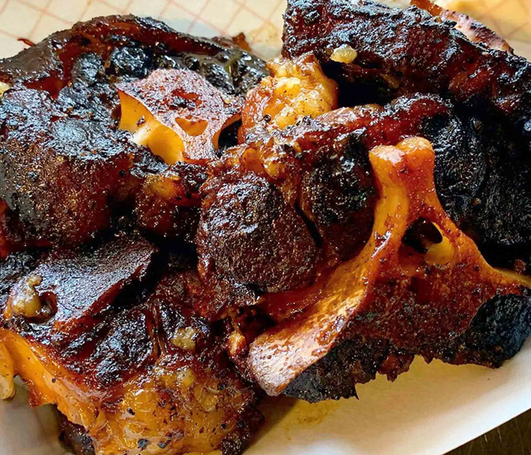 Close-up of smoked beef oxtails with a dark, crispy exterior and visible bones on a serving tray
