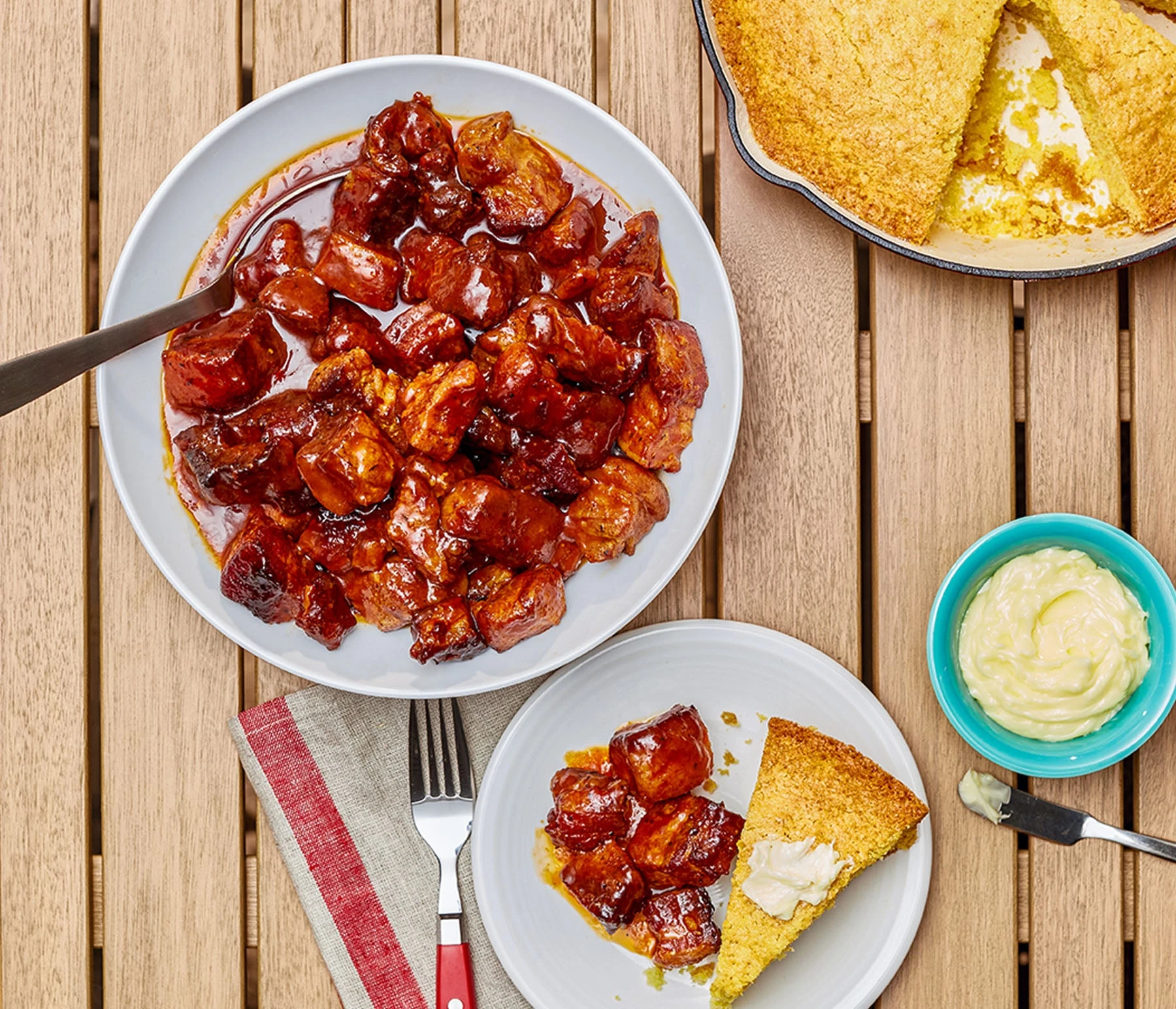Overhead shot of smoked pork belly burnt ends on a plate with other plates of food on a table