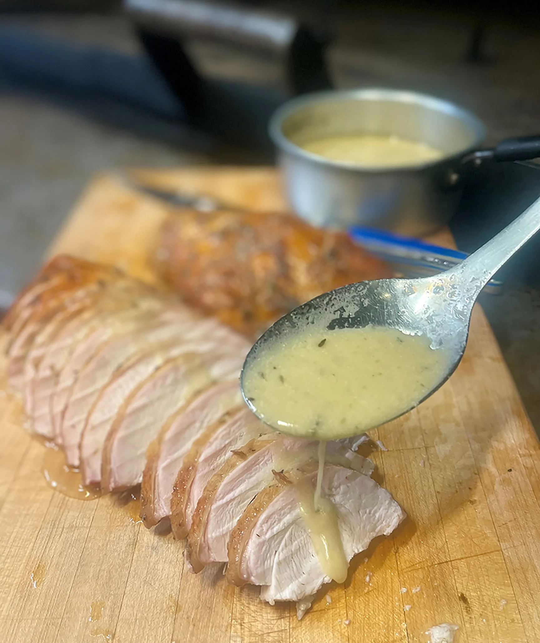 Sliced smoked turkey on a wood cutting board, white gravy being poured over it with a spoon