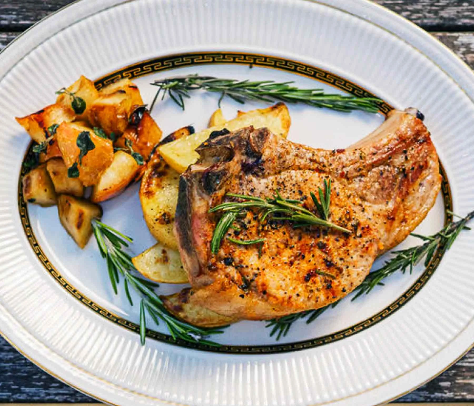 Rosemary, fennel and chili flake rubbed pork chop on a plate with grilled apples