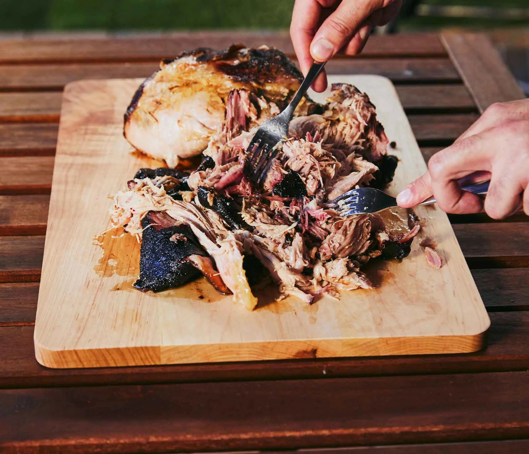 Person cutting up pulled pork on a wood cutting board with forks