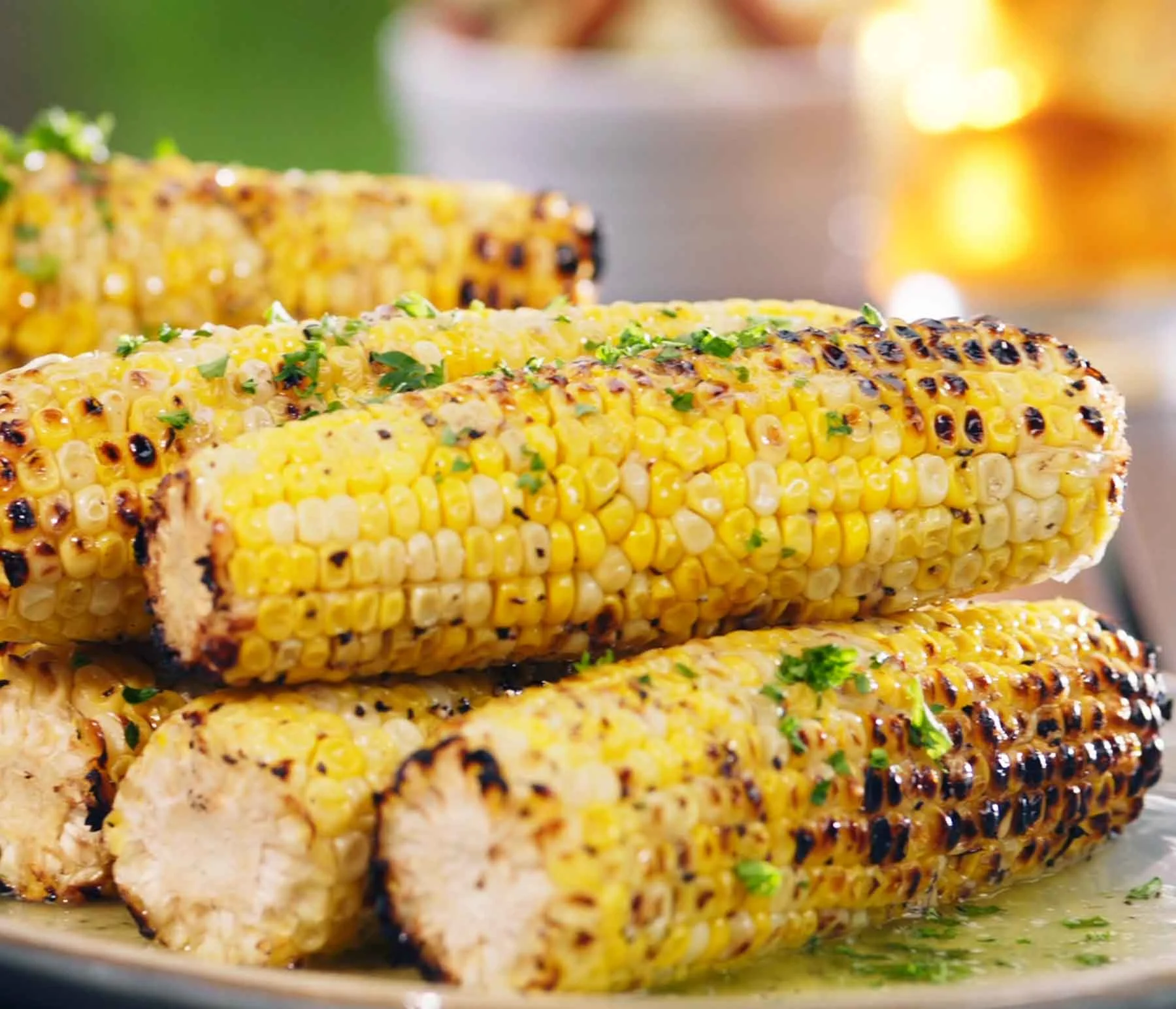 Charcoal-grilled corn on the cob with golden kernels and char marks, topped with melted butter and fresh herbs on a plate