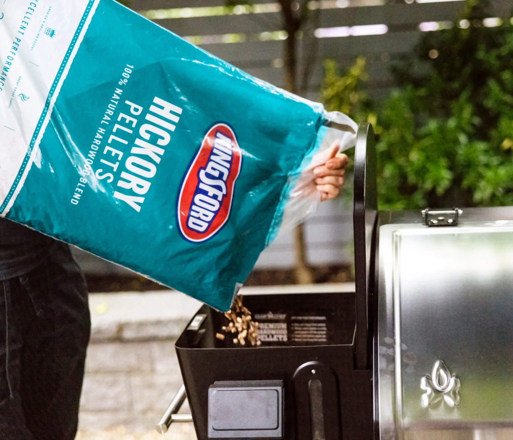 Person pouring Kingsford Pellets into a pellet grill
