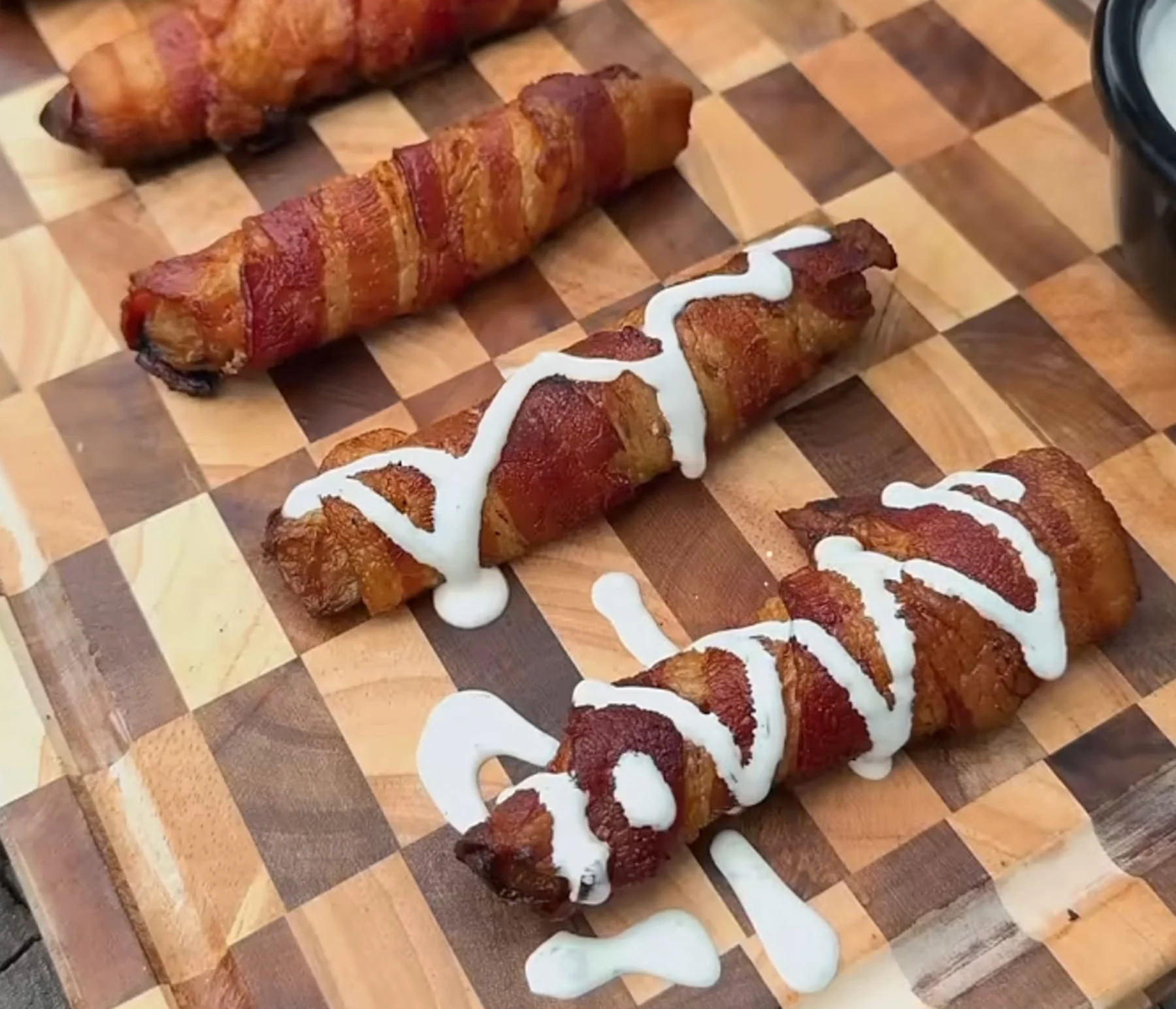 Bacon-wrapped pickle spears drizzled with creamy sauce on a wooden cutting board