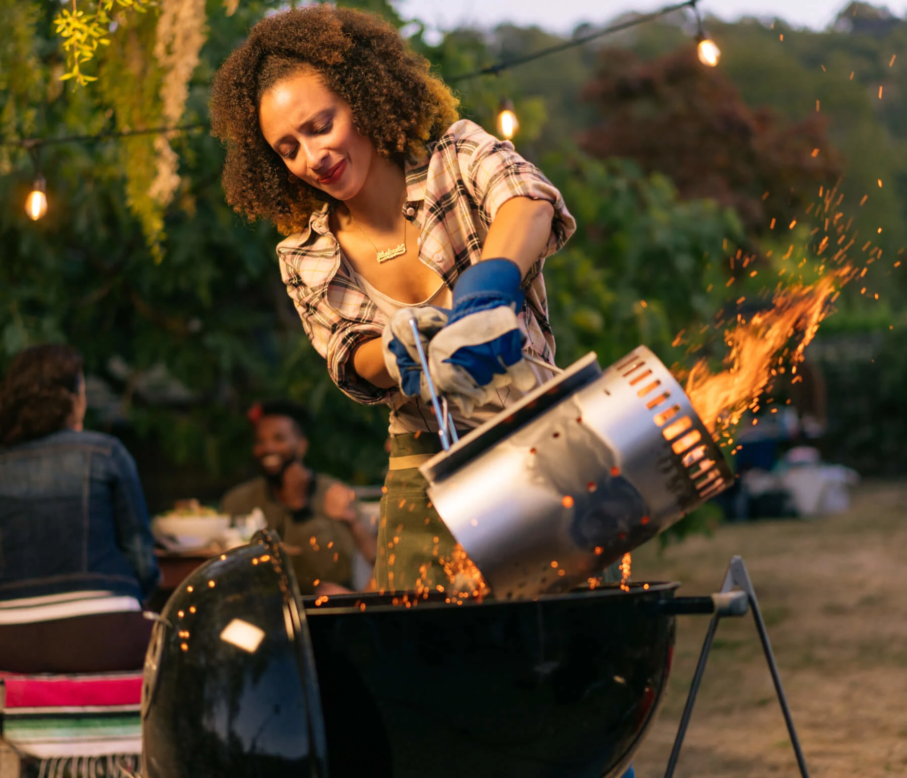 Woman pouring flaming coals from a charcoal starter into a grill