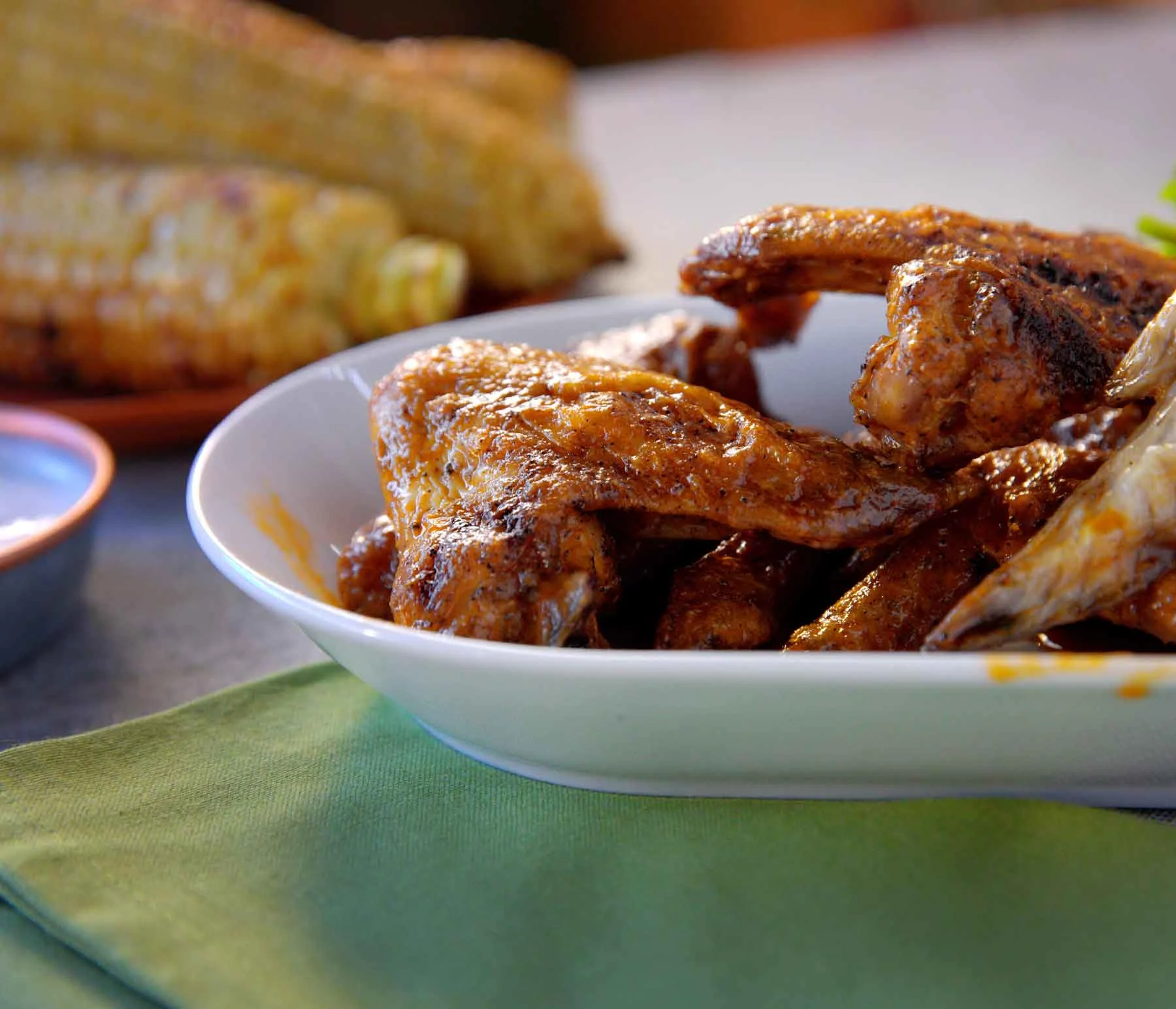 Grilled buffalo wings in a white plate with corn on the cob in the background