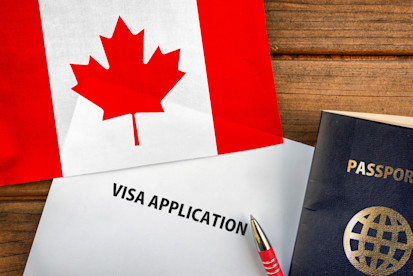 A passport, the flag of Canada and a sheet of paper featuring the words 'visa application' rest on a table