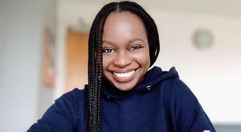 Sarah Lavender Achieng smiles while sat wearing a navy hoodie with a pink floral design on its left arm