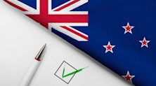 Graphic featuring a green checkmark and a pen on a white background, all of which is down to the left of a section of the New Zealand flag