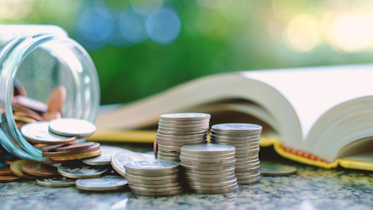 Pile of money, coins in and outside a glass jar