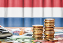 Graphic representing Netherlands tuition fees, with many Euro coins and notes placed on a table with a calculator in front of the Dutch flag