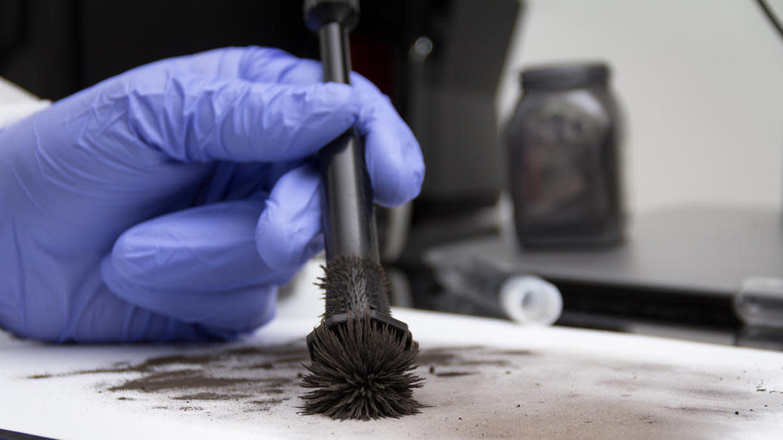 Forensic scientist's gloved hand using a black brush to look at black powdery evidence