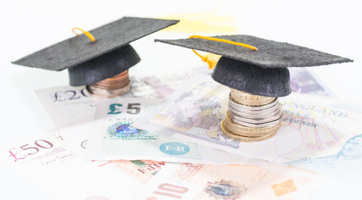Two graduation caps rest on piles of coins that stand over various UK banknotes