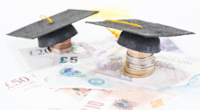 Two graduation caps rest on piles of coins that stand over various UK banknotes