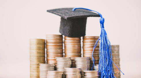 Miniature graduation cap stands on top of one of several piles of coins