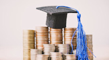 Miniature graduation cap stands on top of one of several piles of coins