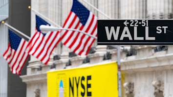 Road sign saying 'Wall St' with three USA flags behind