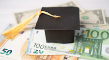 A miniature graduation cap rests on top of several Euro banknotes
