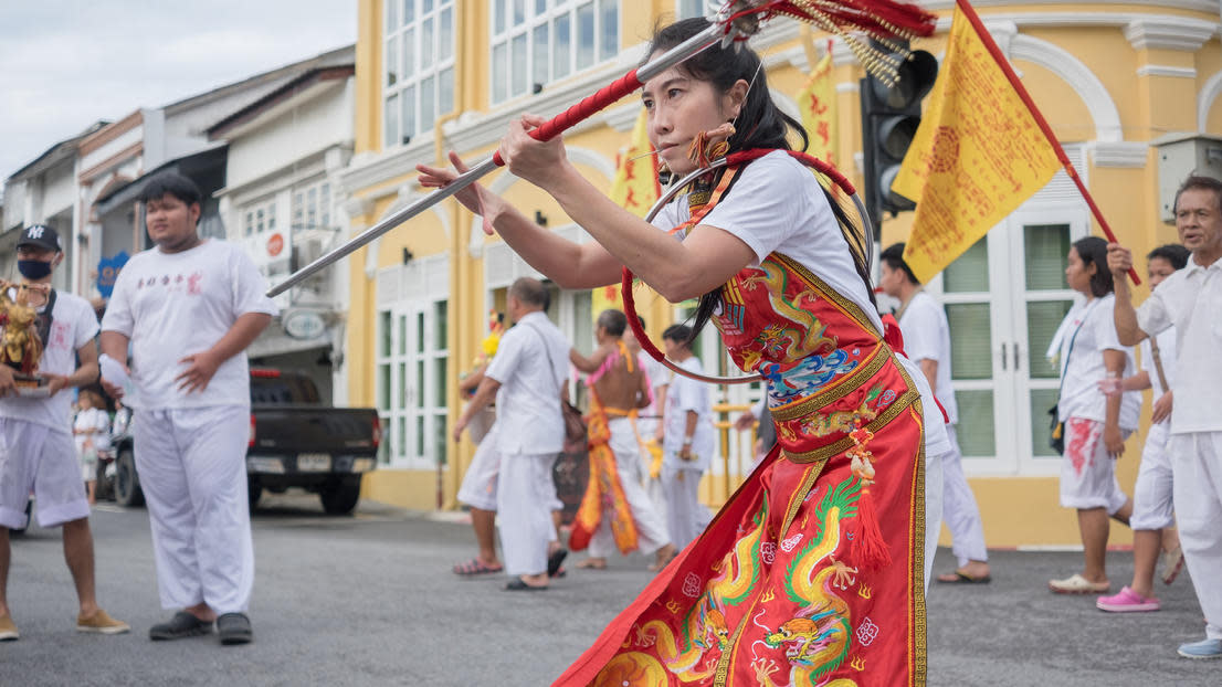 Person dancing in parade in front of yellow building and several people in white clothes